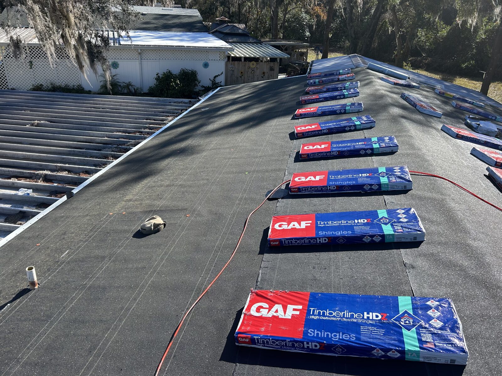 Bundles of GAF architectural shingles staged in a run up a felted roof, an air hose running to the ridge